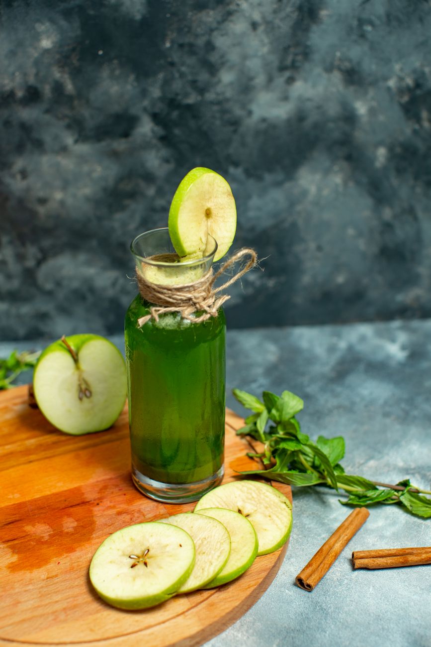 A clear glass of green detox juice with green apples and ginger on the table